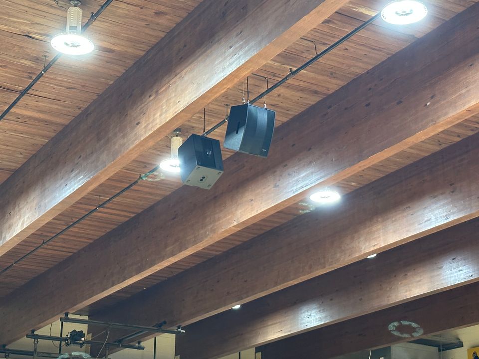 Wide view of the gym from a corner, showing speakers hung between wood beams, championship banners, scoreboard, and the Knights branding.