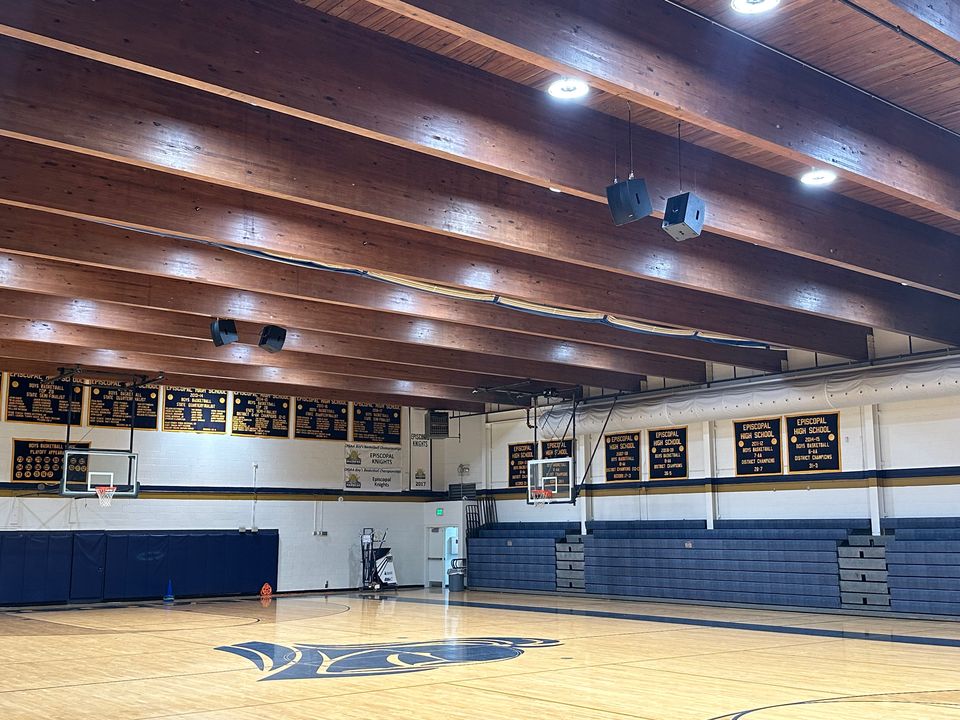 Episcopal High School gymnasium with the Knights logo at center court, championship banners, and Blaze loudspeakers hung from the wood-beam ceiling.