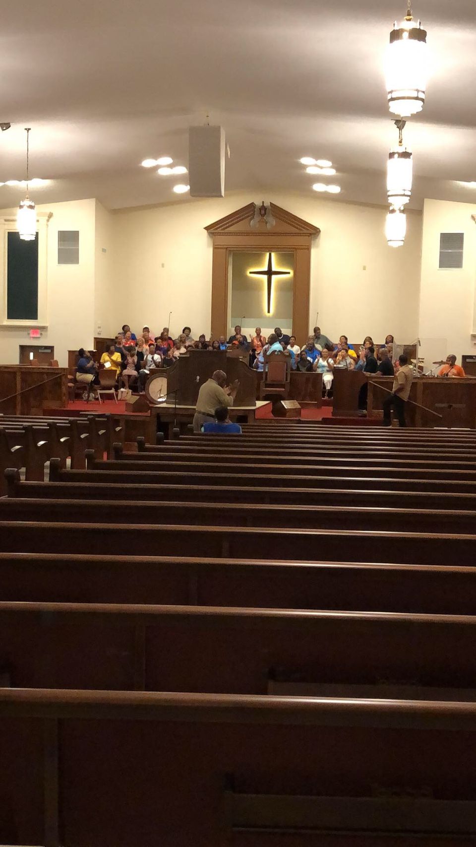Packed Sunday service at Greater Mount Olive Missionary Baptist Church — congregation in the pews, leadership, stained glass, illuminated cross.