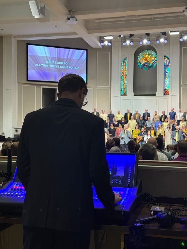 Jefferson Baptist Church Christmas service — robed choir, band, dual side screens, stained-glass cross, wreaths and poinsettias, packed congregation.