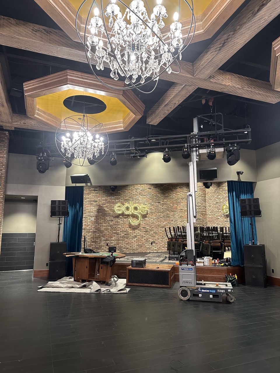Wide install-day shot of the Edge Bar stage with the projector mounting in progress, scaffold in place, the existing laser rig visible.